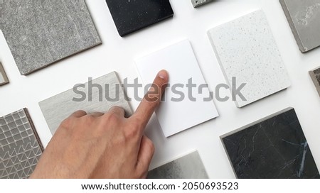 designer's hand choosing samples of interior stone material consists concrete tiles, quartz stones, artificial stones, graphic tile. top view of interior selected material for mood and tone board. 
