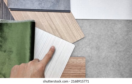 designer's hand selecting to interior material samples containg green velvet fabric, white fabric laminateds, oak wood veneers and concrete vinyl flooring. interior material board for presentation.