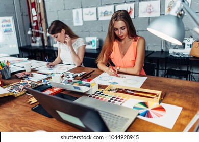 Designers workspace. Two female artists drawing decorative elements sitting at desk in creative studio