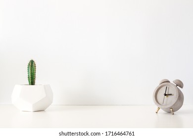 A desk against a white empty wall with a cactus in a geometric pot and a concrete alarm clock. Copy space. - Shutterstock ID 1716464761