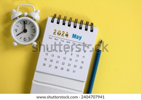 Desk calendar for May 2024 and a small alarm clock on a yellow background