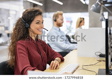 Desk consultant talking on hands-free phone. Smiling call center operator with headset working on support hotline. Busy call center agents working in a modern office, offering customer care service.