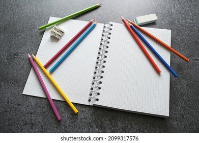 Desk For Creative Work With A Blank Open Spiral Notebook, Crayons, Sharpener And Eraser On A Dark Gray Table, Copy Space, Selected Focus, Narrow Depth Of Field