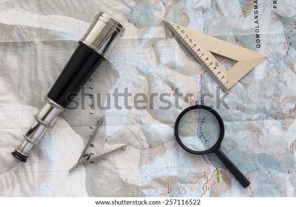 Desk of explorer. Top\
view of desk covered with the topographic map with typical items of\
pioneer-navigator: sea telescope, navigational triangle, magnifier\
and compass