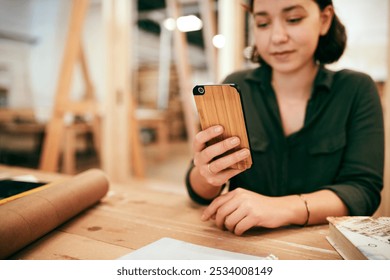 Desk, hand and phone with carpenter woman in workshop for professional joinery or woodworking. Craftsmanship, creative and mobile communication with artisan in industrial warehouse for design update - Powered by Shutterstock