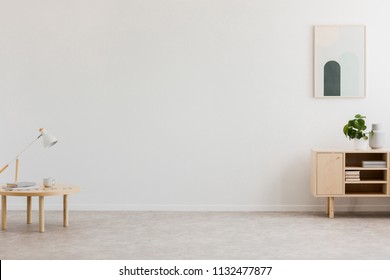 Desk Lamp On A Small Table And A Simple, Wooden Cabinet In An Empty Living Room Interior With White Wall And Place For A Sofa. Real Photo.