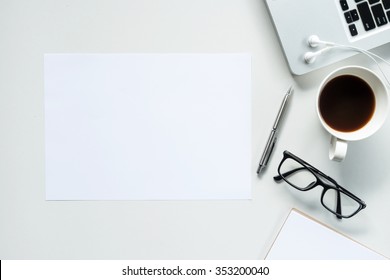 Desk With Laptop, Eye Glasses, Earphone, Pen And A Cup Of Coffee, Top View. The Blank Paper Can Be Used To Put Some Text Or Images.