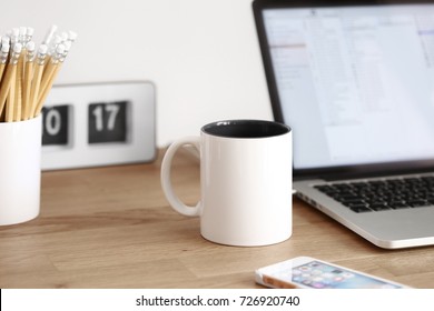 Desk in the morning with mug, laptop, phone, clock, and pens
