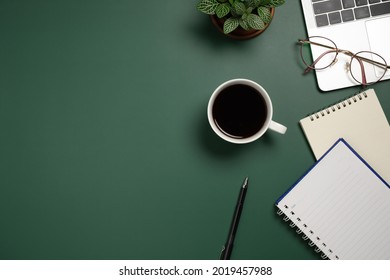 Desk office with laptop, blank notebook, flower, glasses, coffee cup and pen on green table. Flat lay top view copy space. Home office. - Shutterstock ID 2019457988