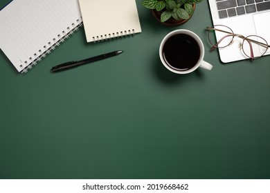 Desk office with laptop, blank notebook, flower, coffee cup, glasses and pen on green table. Flat lay top view copy space. Home office. - Shutterstock ID 2019668462