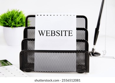 A desk organizer holds a notepad labeled WEBSITE while a small green plant and various office supplies create a tidy workspace. The setting is bright and minimalistic. - Powered by Shutterstock