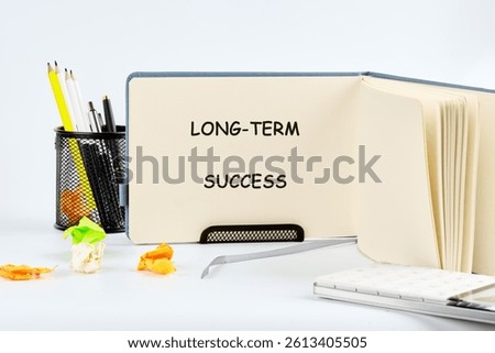 A desk setup features a notebook open to the words long term success, surrounded by colorful stationery and decorative items that inspire motivation and productivity.
