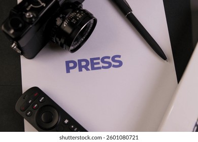 Desk setup featuring press materials, a camera, and a remote control, ideal for media-related activities.