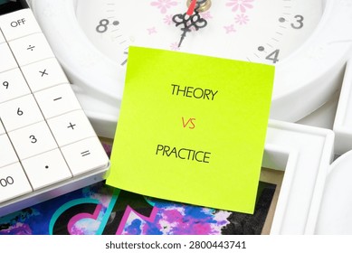 A desk setup includes a calculator and a clock with a colorful sticky note displaying the words theory vs practice. This setup highlights work and study.