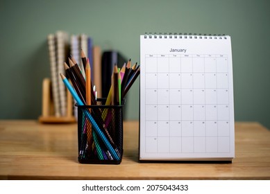 Desk for student education concept. Book, and pencil for study for exam. 2022 Calendar placed on white School table with bookshelf and green wall background for student plan to work at home.