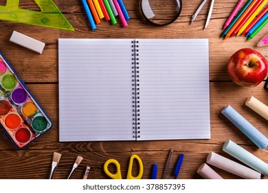 Desk with various school supplies and empty lined paper notebook  in the middle . Studio shot on wooden background, frame composition, empty copy space