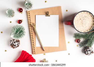 Desktop Blank Note Pad. Flat Lay Of White Working Table Background With Cup Of Coffee And Christmas Decoration. Top View Balls, Fir Tree, Paper Clips, Mock Up Greeting Card, Craft Notebook And Pen.