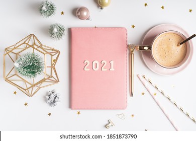 Desktop Christmas notepad with 2021 letters text. Flat lay of white table background with planner, cup of coffee, Christmas decoration and stationery.