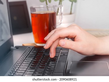 Desktop with a computer, a flower and a cup of tea close-up. The girl's hand presses the laptop key.