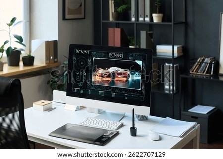 Desktop computer with graphic design software on screen, displaying illustration of racing car in motion, in office of auto engineering company