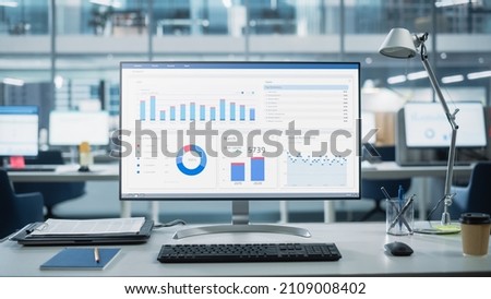 Desktop Computer Monitor with Finance Statistical Data Software and Progressive User Interface Standing on the Desk in the Modern Business Office. In the Background Glass Wall with Big City Office.