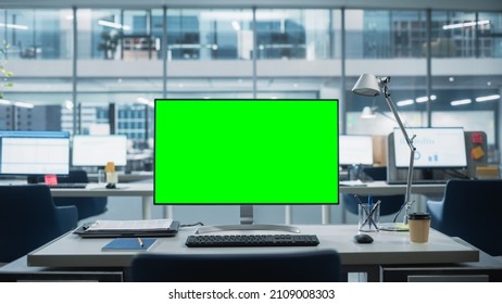 Desktop Computer Monitor With Mock Up Green Screen Chroma Key Display Standing On The Desk In The Modern Business Office. In The Background Glass Wall With Big City Office.