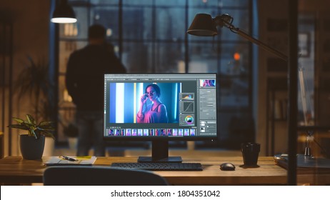 Desktop Computer with Photo Editing Software Standing on the Desk in the Modern Creative Office. In the Background Designer Drinks from a Cup Looks at the Night City out of the Window. - Shutterstock ID 1804351042