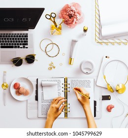 Desktop Flatlay Sceneof A Feminine Workspace, With Open Planner With Hands, Laptop And Gold Feminine Stationery Accessories. Arranged On A Plain White Background.