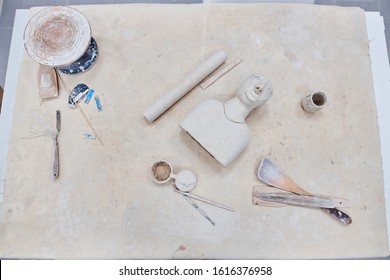 The desktop of the potter’s master, who makes objects from clay and ceramics. Table of the artist, brushes, rolling pin, wood. A young girl is engaged in pottery.