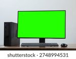 A desktop PC setup with a green screen monitor, keyboard and mouse on a wooden desk against a neutral background.