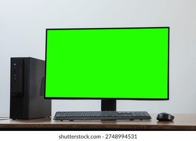 A desktop PC setup with a green screen monitor, keyboard and mouse on a wooden desk against a neutral background.