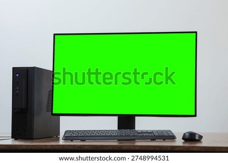 A desktop PC setup with a green screen monitor, keyboard and mouse on a wooden desk against a neutral background.