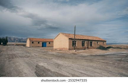 Desolate scene with rustic brick buildings, blue doors, and moody sky casting shadows on dusty foreground. - Powered by Shutterstock