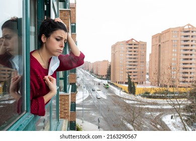 Despair Bored Woman Under Covid 19 Quarantine Looking Out The Window For Breaathing Clean Air During A Cold Winter Snow Storm In The City.