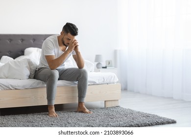 Despair Concept. Portrait Of Depressed Young Arab Man Sitting On Bed At Home, Upset Middle Eastern Man Leaning Head On Hands, Having Life Problems, Feeling Heartbroken And Lonely, Copy Space
