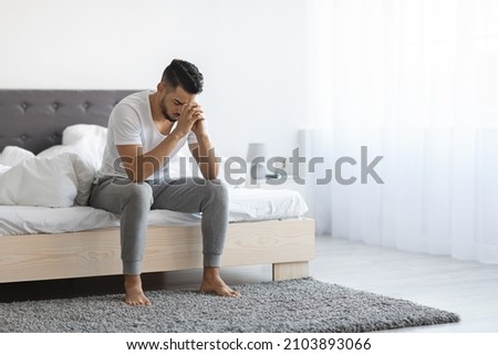 Despair Concept. Portrait Of Depressed Young Arab Man Sitting On Bed At Home, Upset Middle Eastern Man Leaning Head On Hands, Having Life Problems, Feeling Heartbroken And Lonely, Copy Space