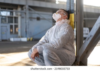 Despair Healthcare Worker In White Covid Protective Overalls.Tired Male Caucasian Doctor Grabs His Head Cower In Depression During Coronavirus Pandemic Paramedic Overworked Cry Covered Face With Hands