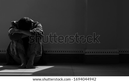 Despair Sorrow Person is Sitting Alone and Hugging his Knees on the floor with Light and Shadow in Empty Dark Room, Black and white style