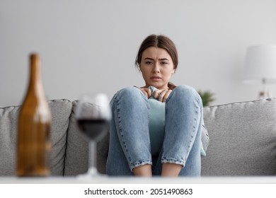Despaired sad caucasian millennial lady with glass and bottle of wine suffering from depression and stress at home. Fear, alcohol addiction, worries and loneliness, self-isolation and mental health