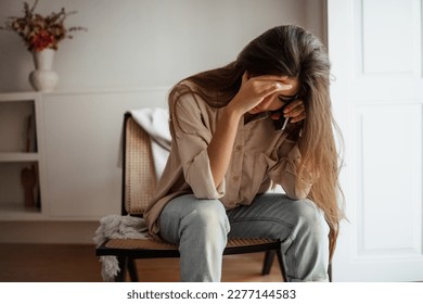 Despaired sad millennial mixed race female calls by phone, talks, sits on chair, suffering from bad news in room interior, free space. Communication remotely, problems, stress at home - Powered by Shutterstock