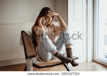Despaired sad pensive millennial european lady calling by smartphone, talking, sit on chair in minimalist room interior. Loneliness, reaction to bad news, gossip, stress at home