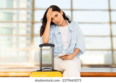 Despaired unhappy millennial european woman with suitcase and passport, suffers from late for transport, sit on train station or airport. Problems and stress, travel mistake emotions - Shutterstock ID 2379663073