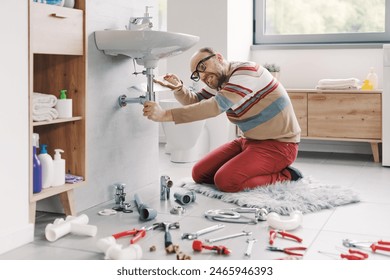 Desperate angry man trying to fix the bathroom sink, he is sawing the drain pipe - Powered by Shutterstock