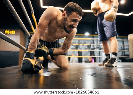 Desperate athlete staying on his knees before the opponent leaning on the floor with his right hand