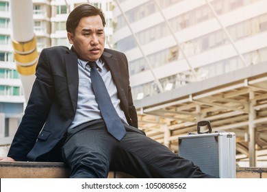 Desperate businessman sitting hopelessly on stair floor in central business district due to unemployment. Concept of failure, desperation, unemployment and business depression. - Shutterstock ID 1050808562