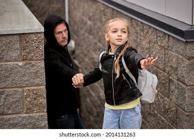 desperate child girl need help, kid is kidnapped by pedophile on street, male pedophile take girl's hand, commit crime. abuse concept. caucasian child girl spread arms forward calling people, help