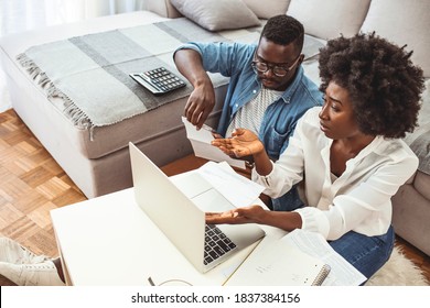 Desperate Couple Doing Their Accounts In The Living Room. Serious African American Couple Discussing Paper Documents, Sitting Together On Couch At Home, Man And Woman Checking Bills