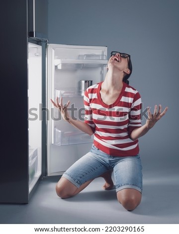Desperate crying woman and empty fridge, she is hungry but she has no food at home