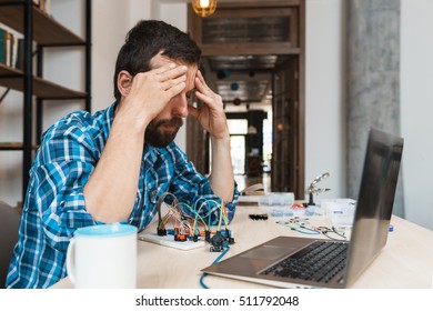Desperate engineer sitting near laptop and electronic construction. Failed connection, broken details, unsuccessful experiment
