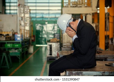 Desperate, Frustrated Tired Of Overwork Asian Man Sitting On Heavy Machinery In The Factory Losing All Money. Worried Stressed Businessman In Suit Shocked By Bad News In His Sme Industry At Work.